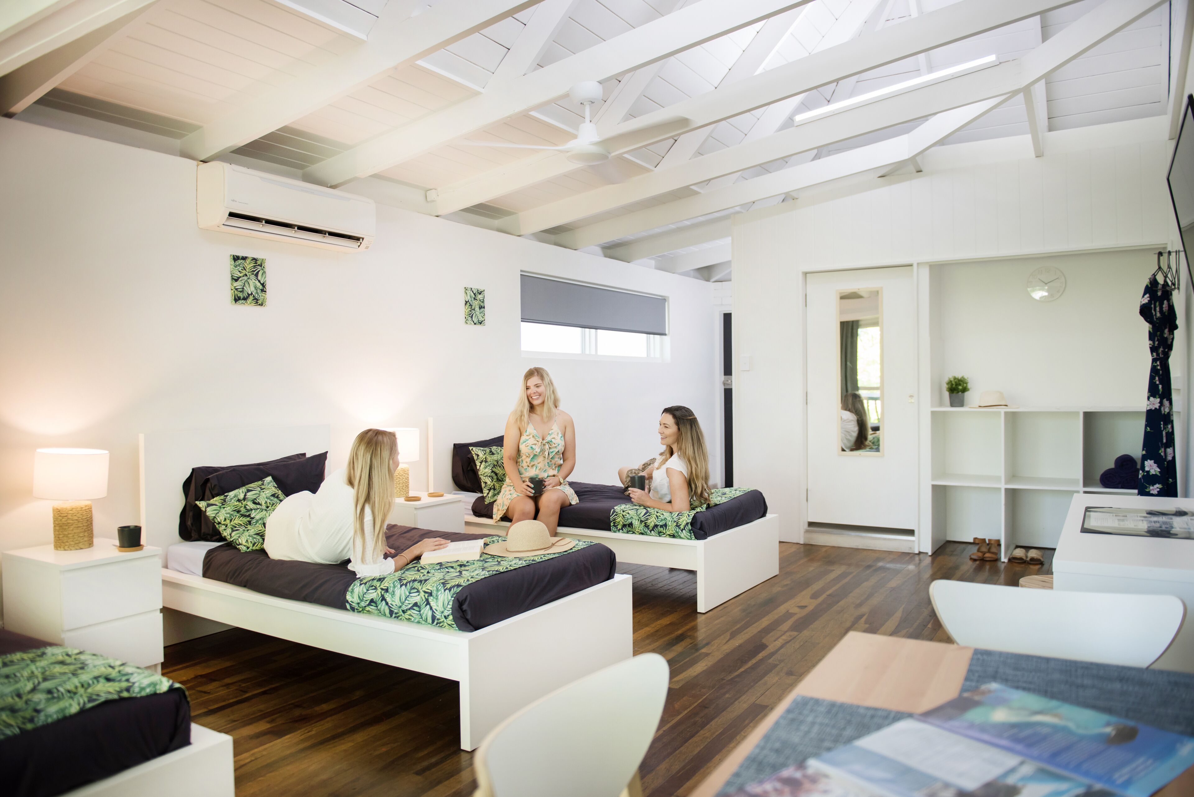 Una habitación moderna y bien iluminada, con techo alto, paredes blancas y tragaluz. Hay dos sofás blancos con cojines oscuros, una mesita y una silla blanca.
