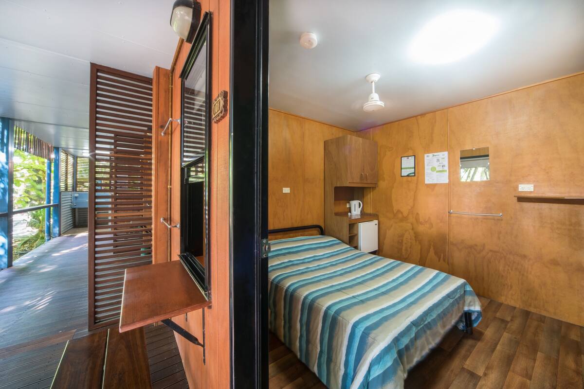 Een slaapkamer met een bed, houten wanden, een klein kastje en een raam.