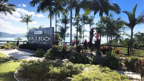 Schild mit der Aufschrift 'AIRLIE BEACH HEART OF THE REEF', im Hintergrund Palmen und der Blick auf das Meer.