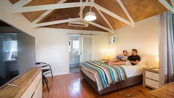A bedroom with a wooden ceiling, a bed with striped bedding, a bedside table, and a nightstand.