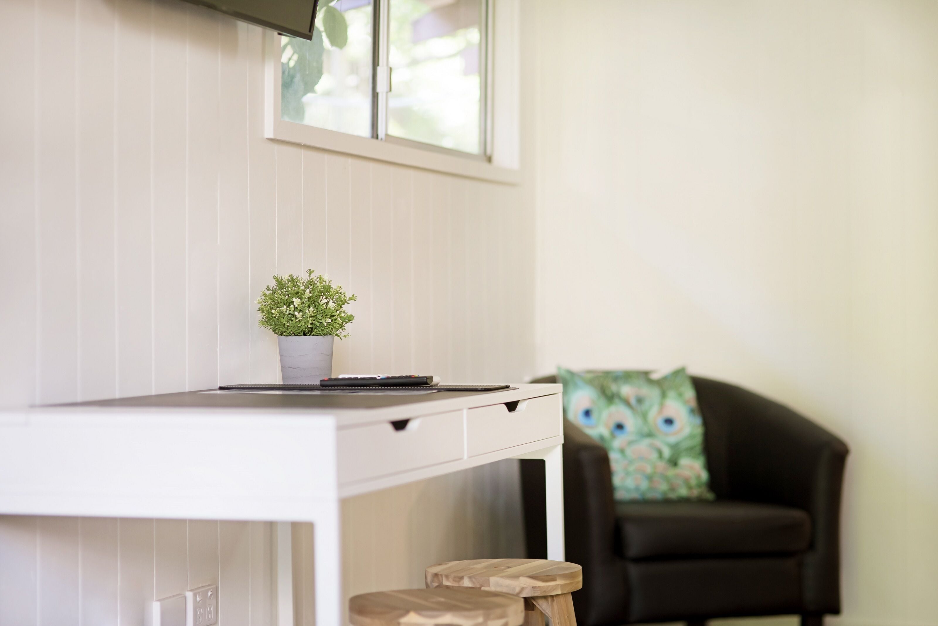 A white desk with a potted plant, a laptop, and a black chair with a colorful pillow.