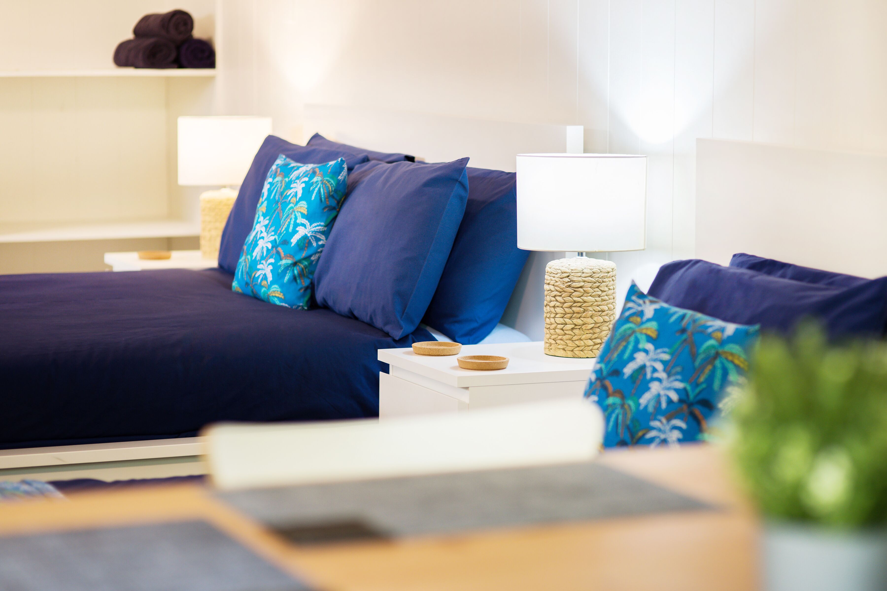 A neatly arranged bedroom with a bed, pillows, a bedside table with a lamp, and a small plant.