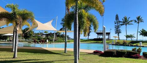 A pool area with palm trees, a covered seating area, and a clear blue sky.