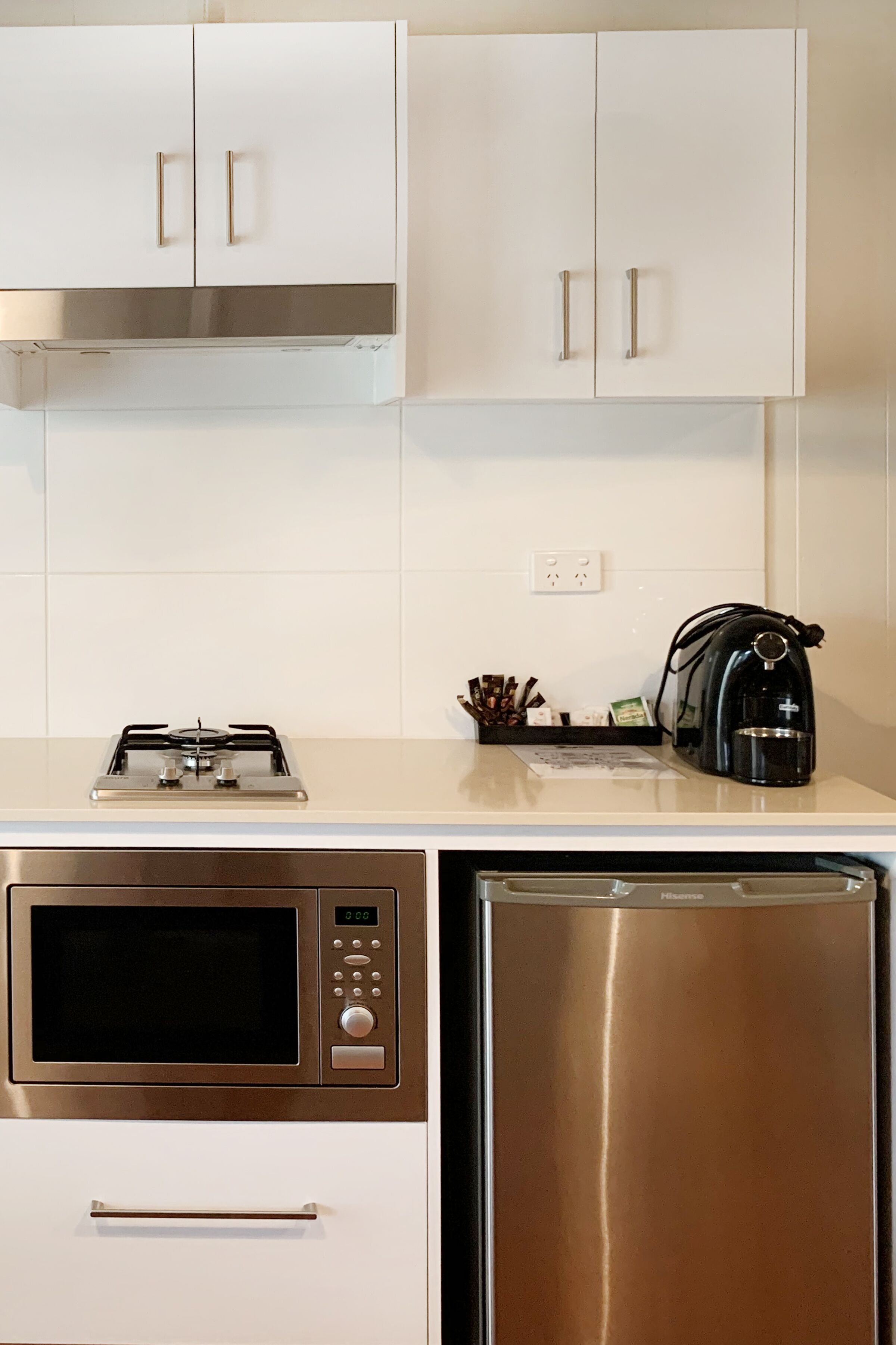 A kitchen with white cabinets, a microwave, a dishwasher, and a kettle on the countertop.