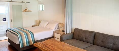 A bedroom with a bed, a wooden bench, a gray sofa, and a nightstand with a lamp.