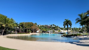 Ein großer Pool, umgeben von Palmen und einem Sandstrand.
