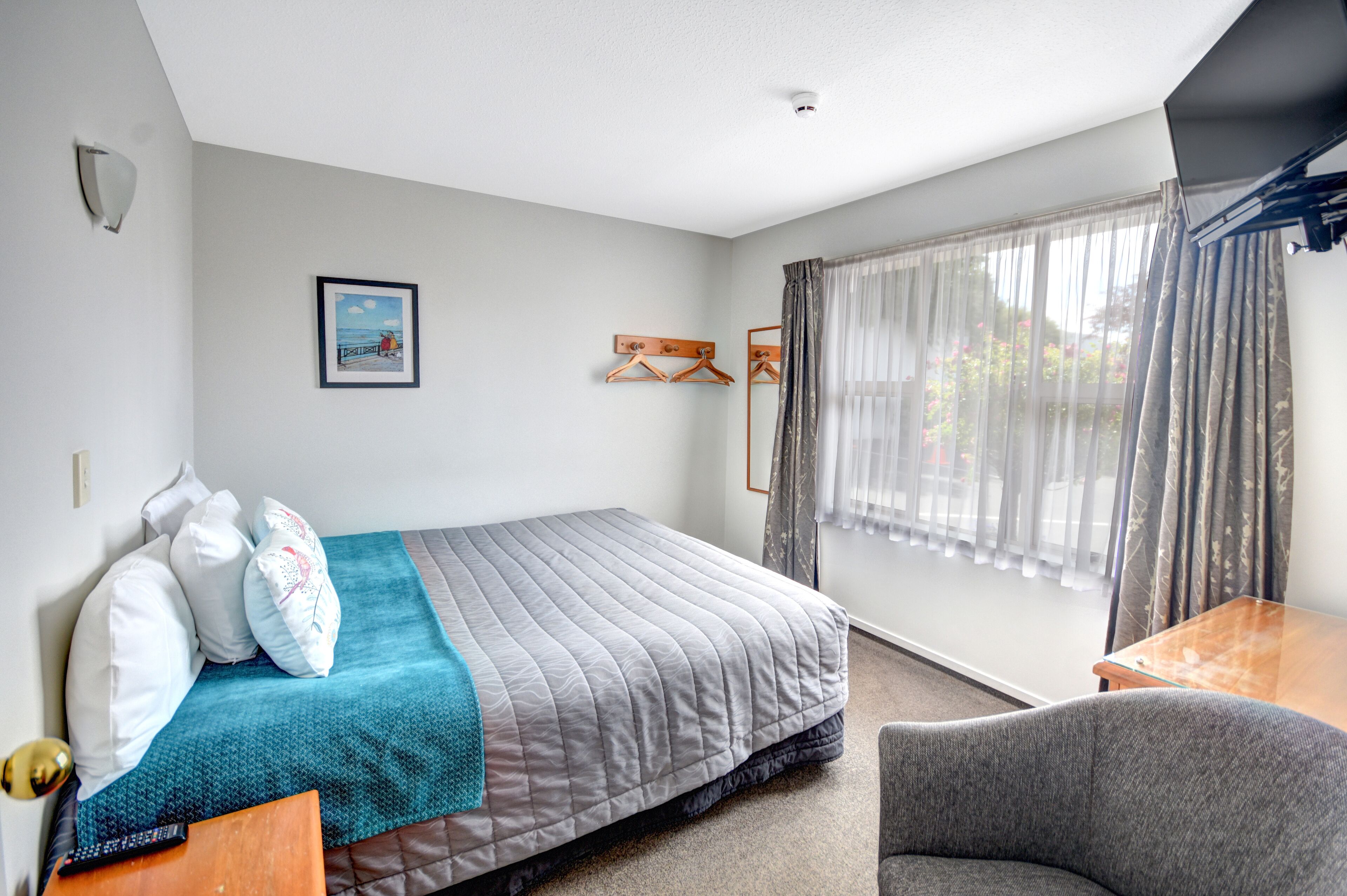 A neatly arranged bedroom with a bed, a chair, a small table, and a window with curtains.