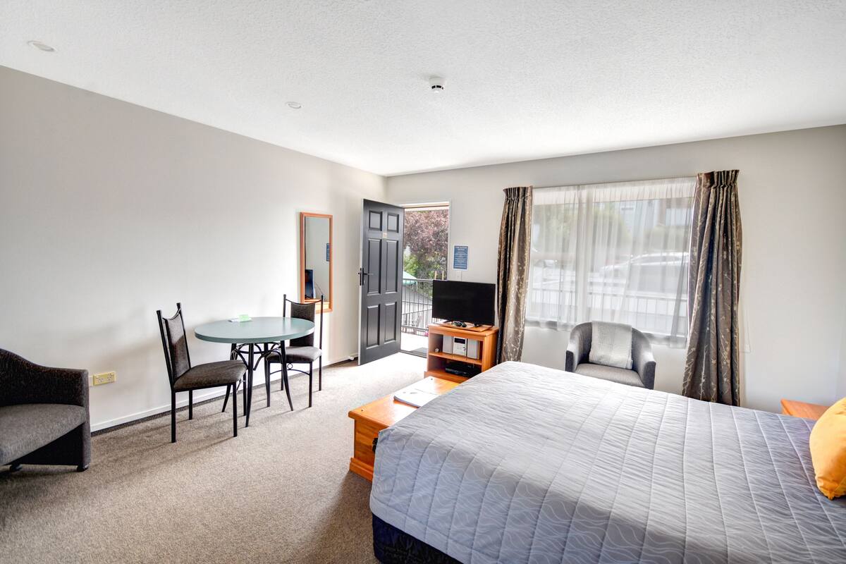 A hotel room with a bed, a desk, a chair, a television, and a window with curtains.