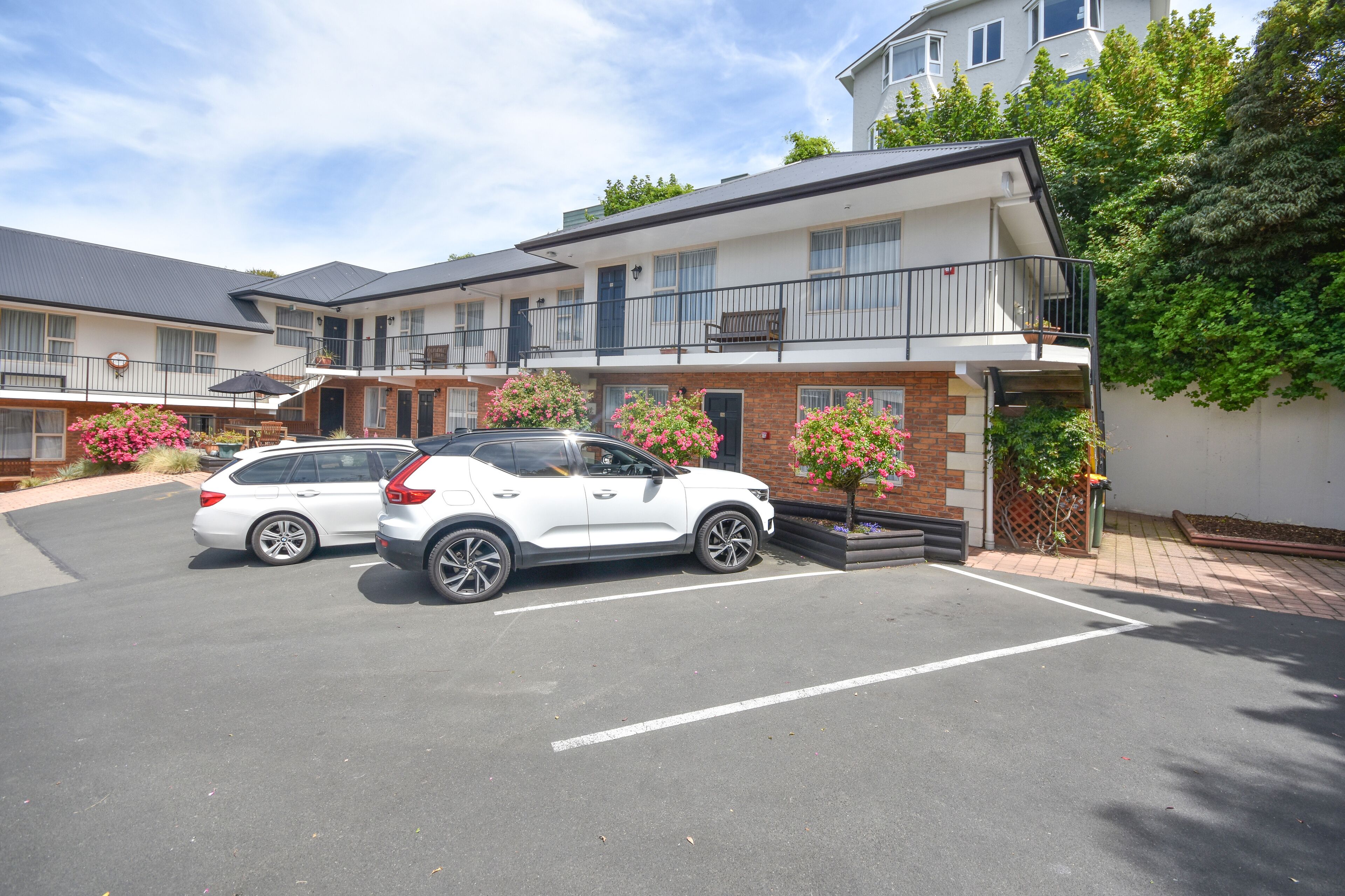 A parking lot with two white SUVs parked in front of a building with a brick facade and balconies.