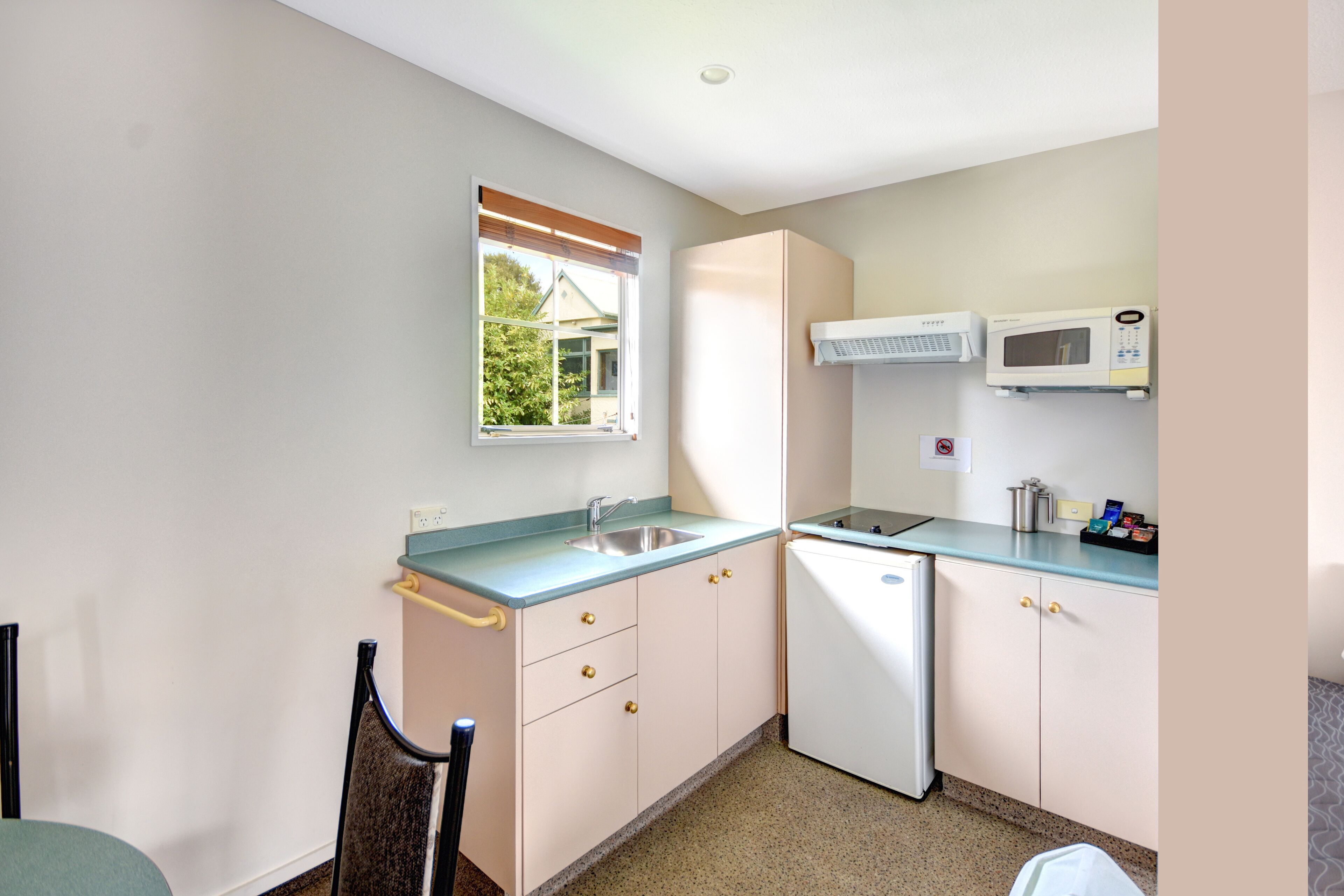 A compact kitchen with a sink, microwave, and a window with a view of greenery.