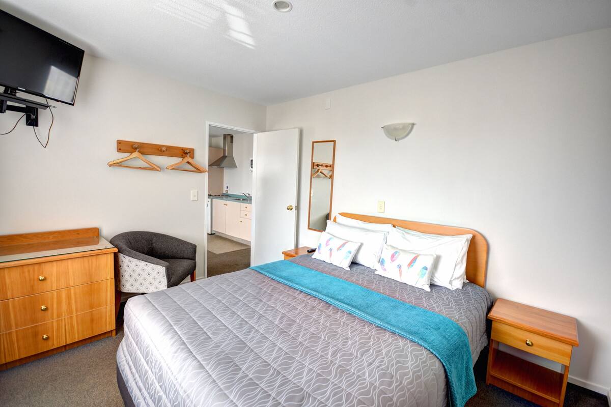 A neatly arranged bedroom with a bed, dresser, and a television mounted on the wall.