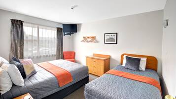 Habitación de hotel con dos camas, una mesita de noche de madera, un televisor montado en la pared y una ventana con cortinas.