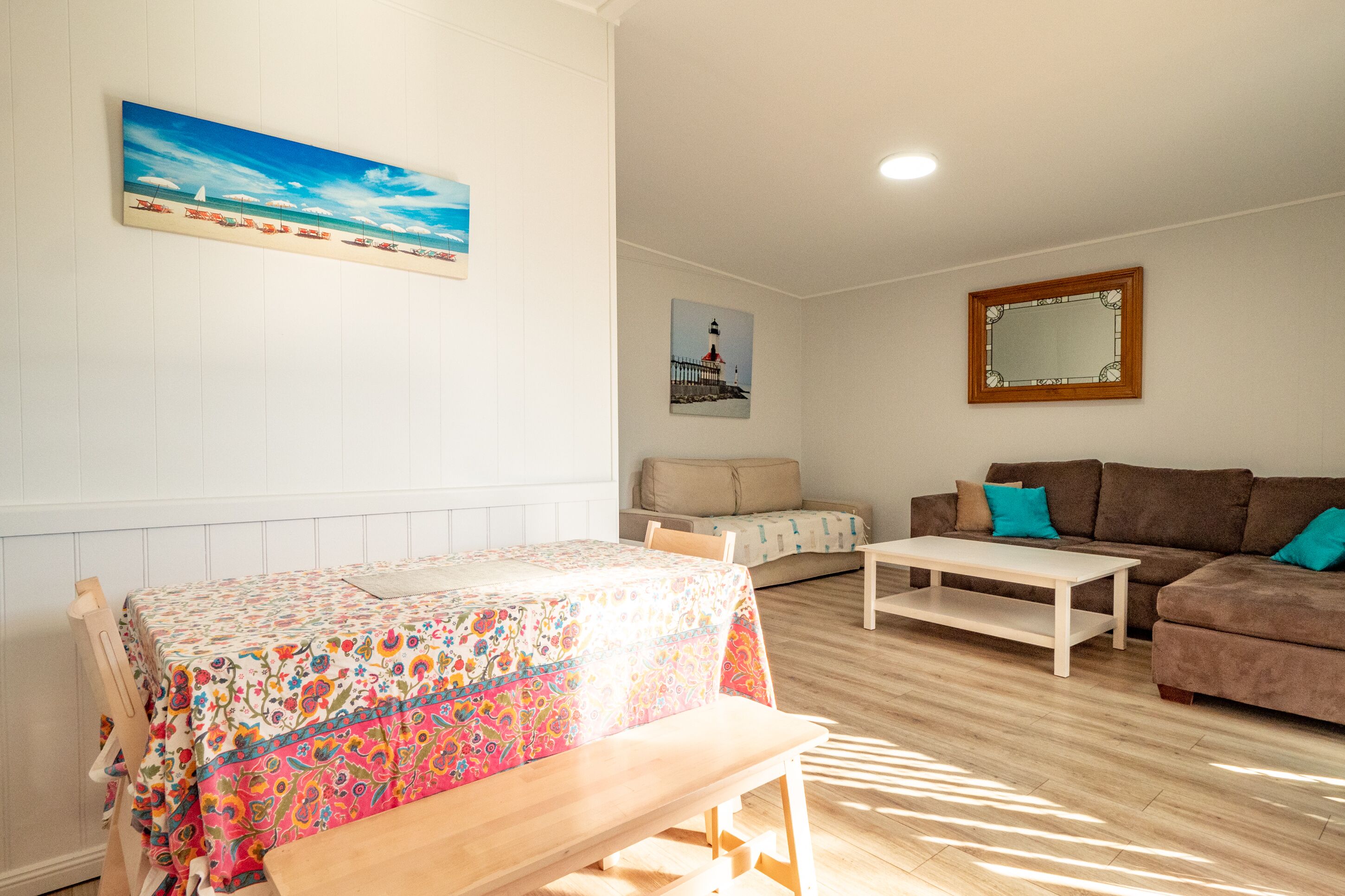 A living room with a wooden floor, a sofa, a small table, a bench, and a colorful tablecloth.