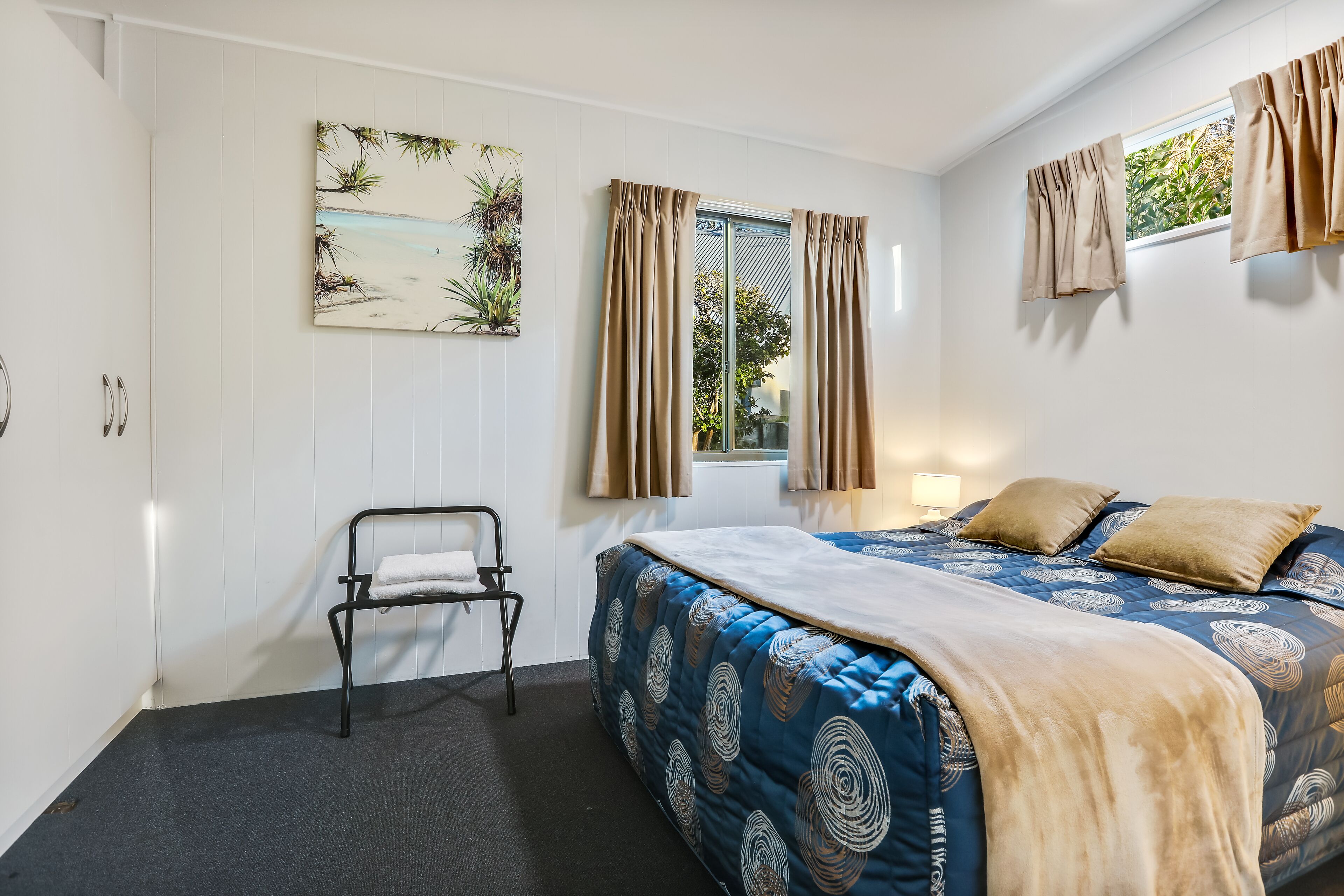 A bedroom with a bed, a chair, a window with curtains, and a painting on the wall.