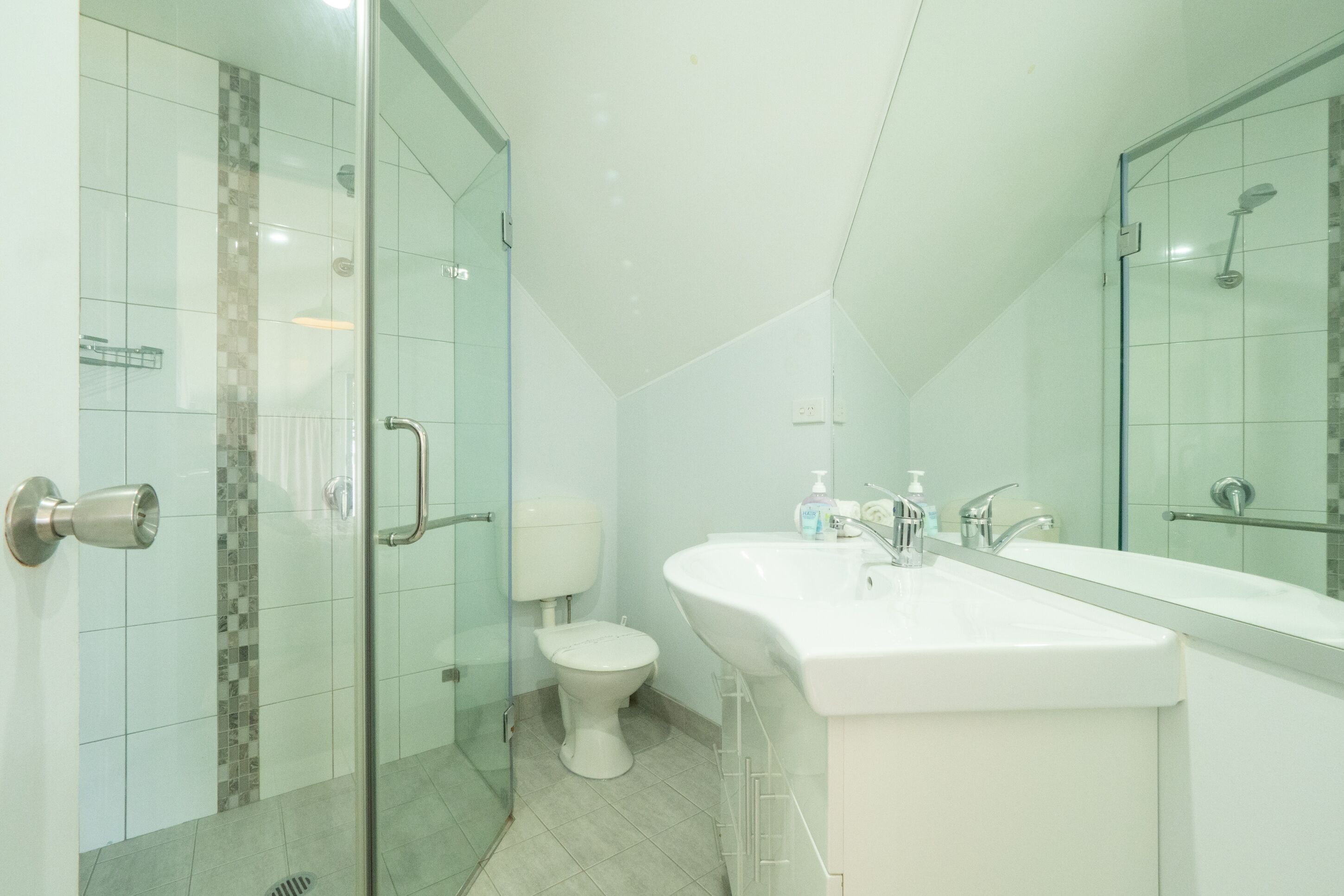 Un baño moderno con cabina de ducha de vidrio, inodoro y un lavamanos grande con espejo superior.