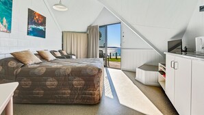 A bedroom with a large bed, a desk, and a view of the sea through an open door.