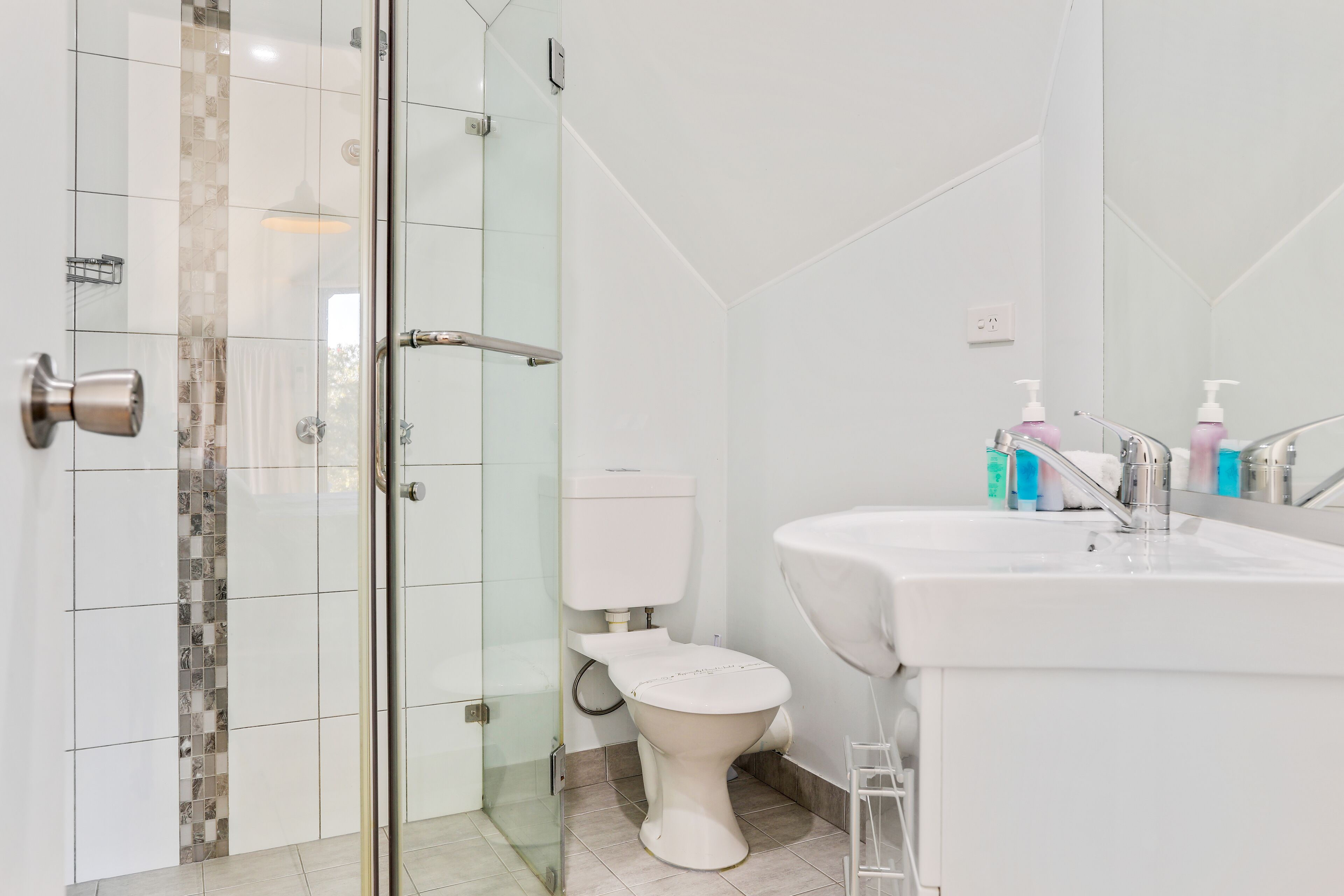 A modern bathroom with a glass shower enclosure, a white toilet, and a sink with a mirror.