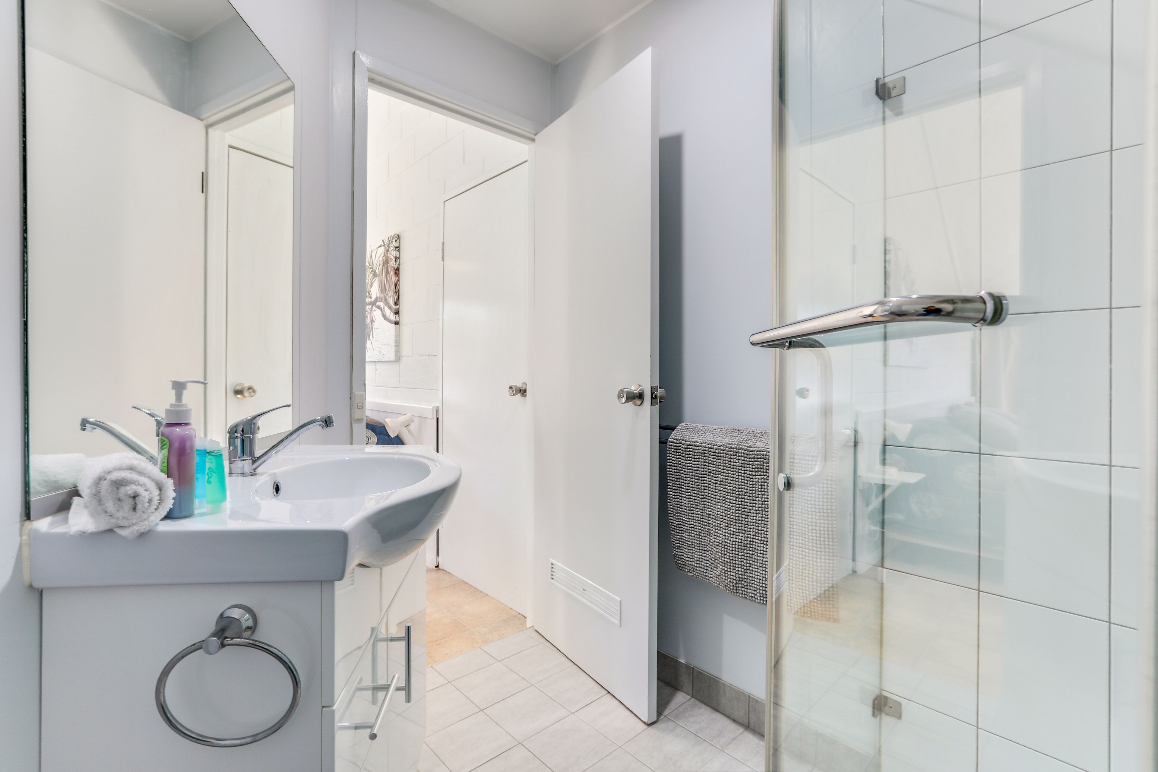 A modern bathroom with a white sink, mirror, and glass shower enclosure.