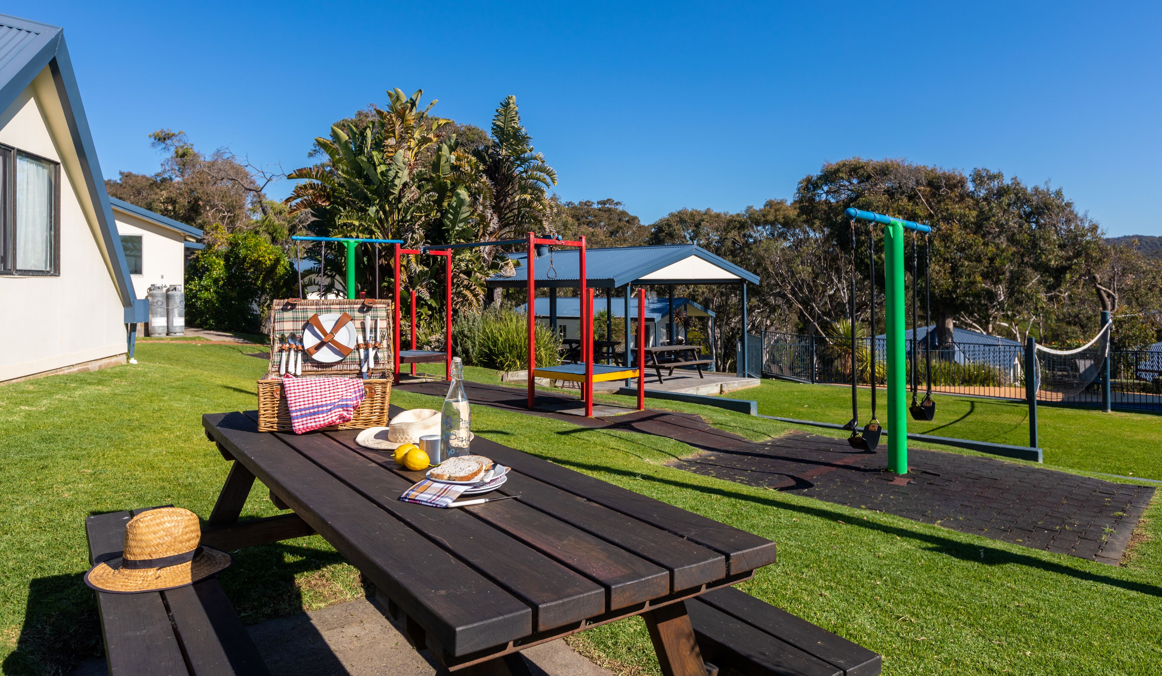 A picnic setup with a table, picnic basket, and outdoor play equipment.