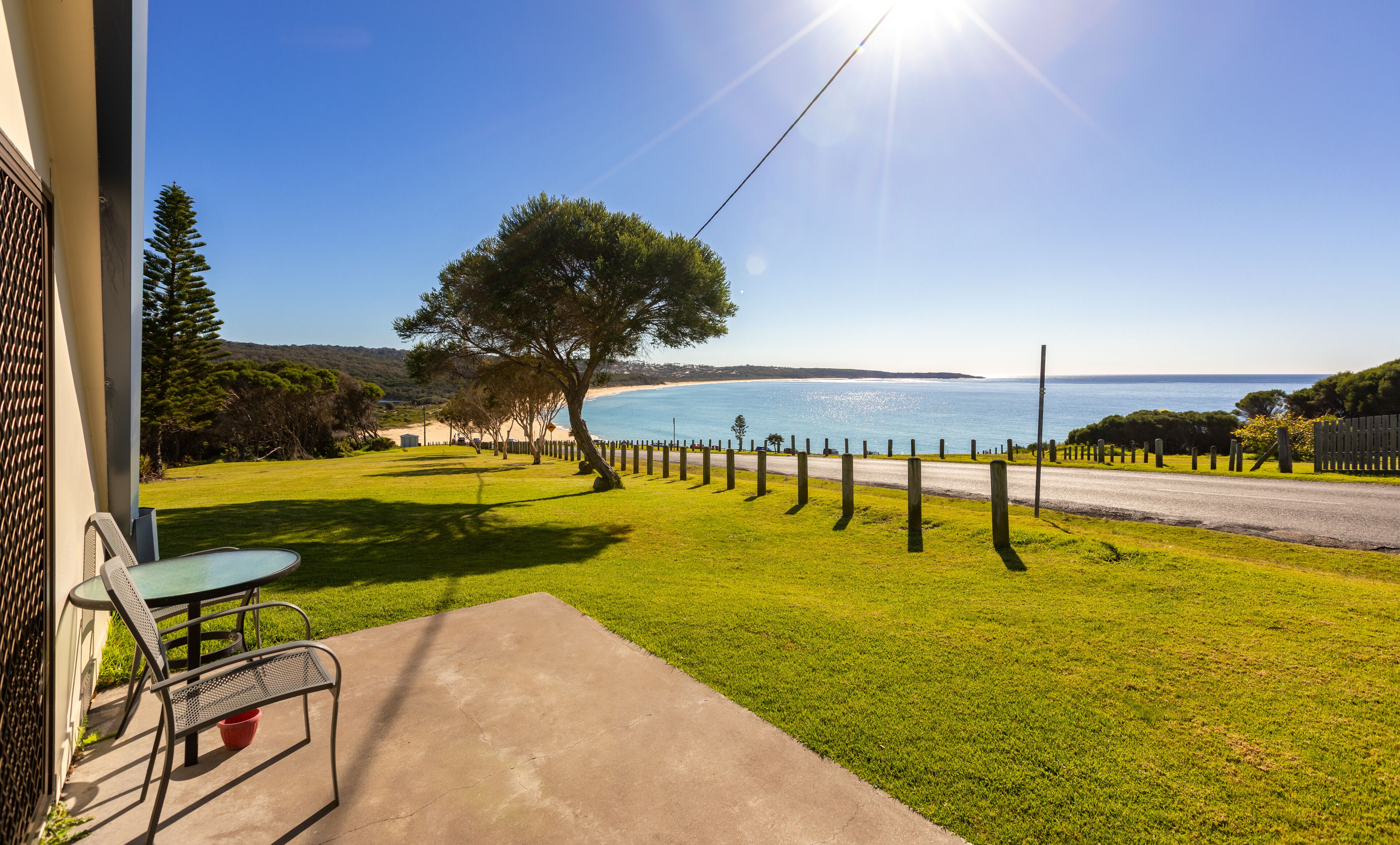 A patio with a table and chairs, a tree, and a view of the sea.