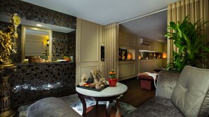 Una sala de estar con un sofá, una mesa de centro con objetos decorativos, un espejo y una cocina al fondo.