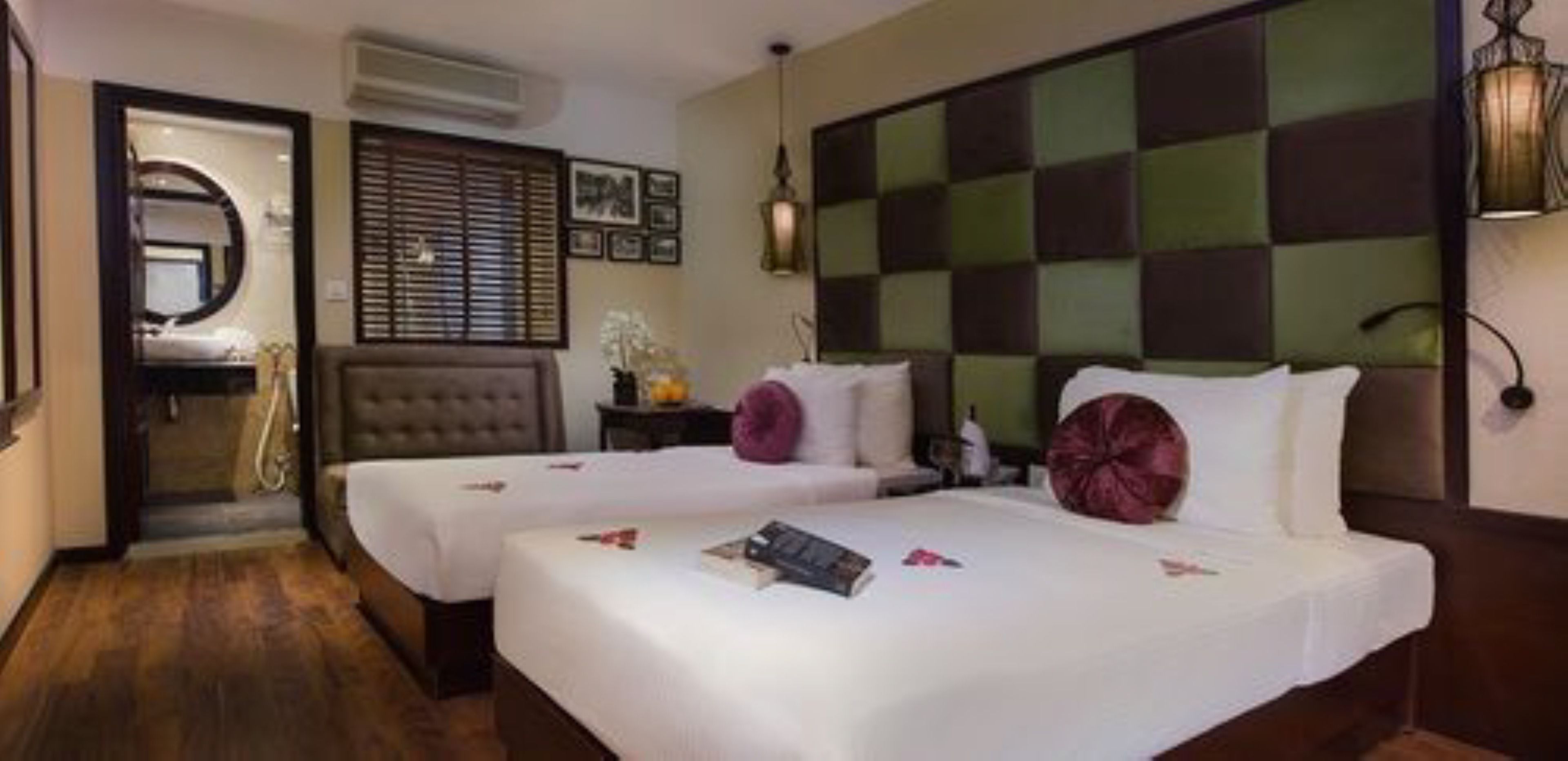 A hotel room with two beds, a bathroom with a mirror, and a check-in counter.