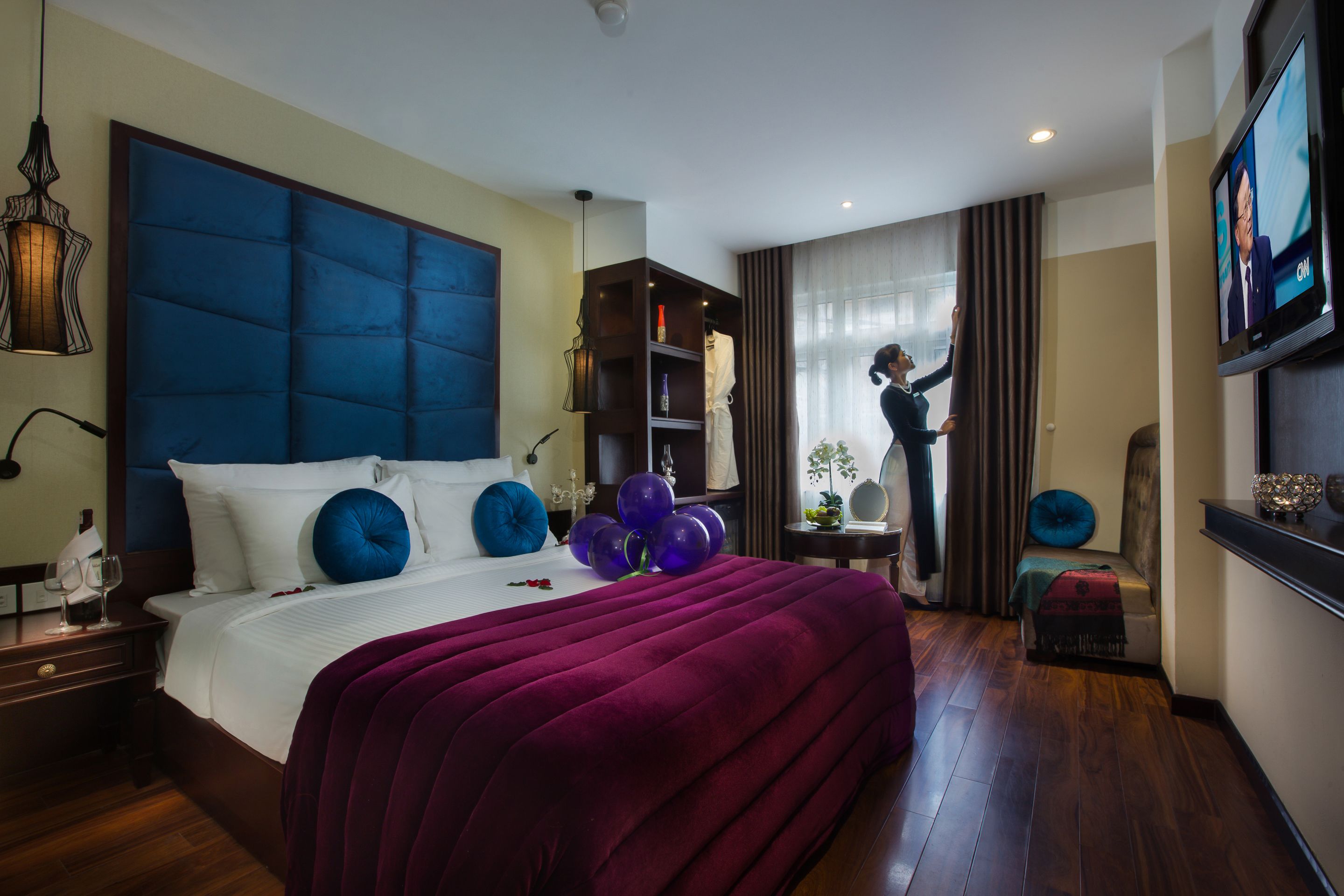 A hotel room with a large bed, a wardrobe, a television, and a seating area with a view of the outdoors.