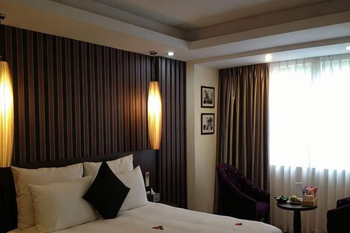 A hotel room with a large bed, a small table, a chair, and a window with curtains.