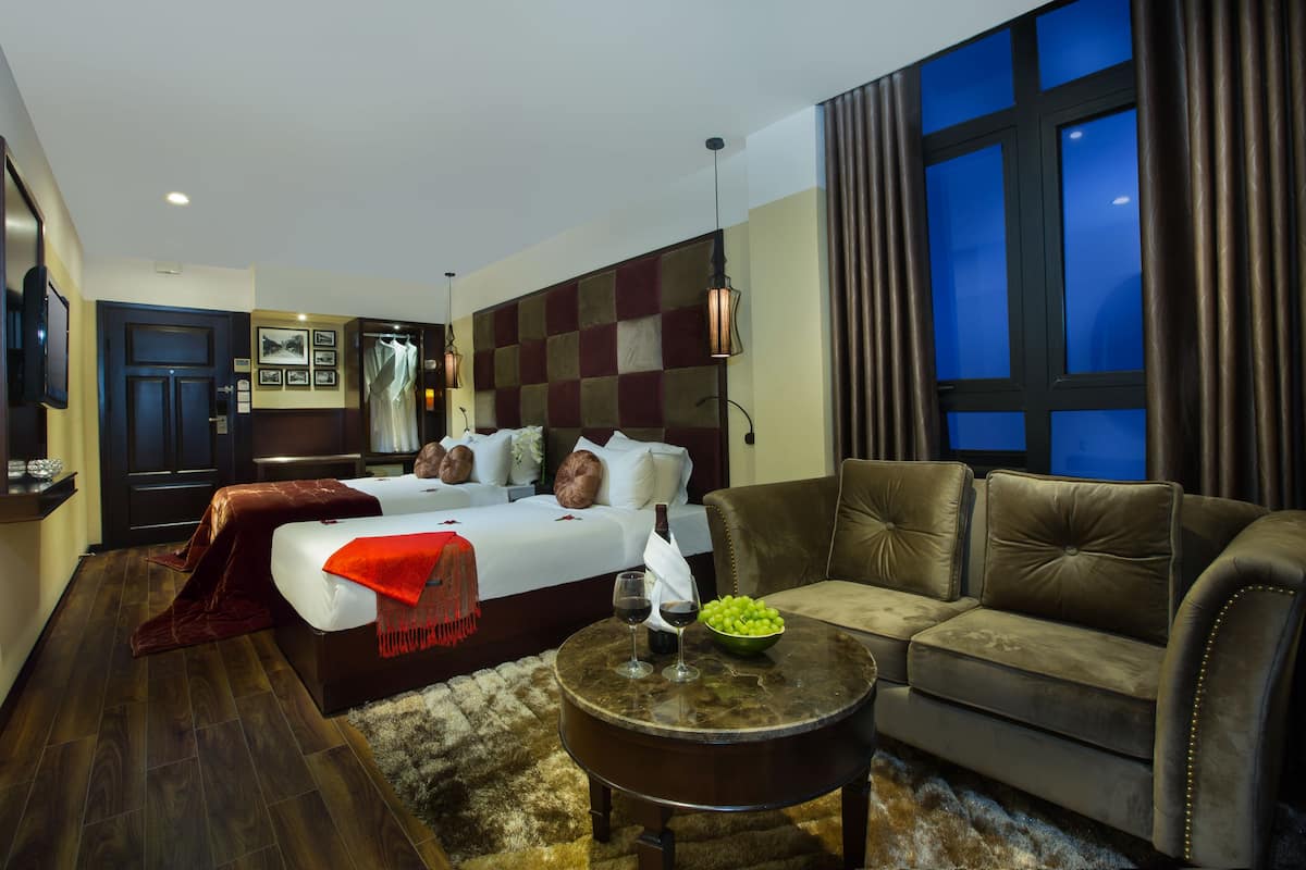 A hotel room with a bed, a sofa, a round coffee table, and a large window with curtains.