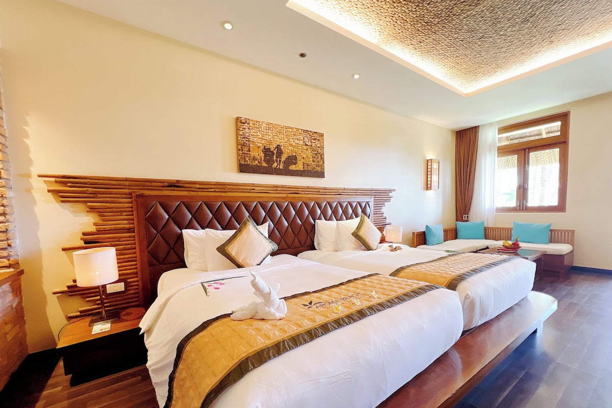 A hotel room with a large bed, a wooden headboard, a nightstand with a lamp, and a painting on the wall.