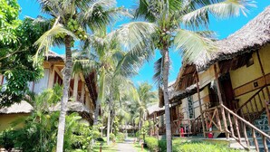 A pathway lined with palm trees and traditional thatched-roof buildings, suggesting a tropical resort setting. - Aroma Beach Resort & Spa (Phu Thuy)