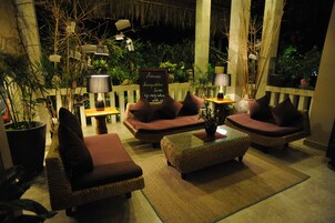Un rincón al aire libre acogedor con muebles de mimbre, sillas acolchadas y una mesa central.