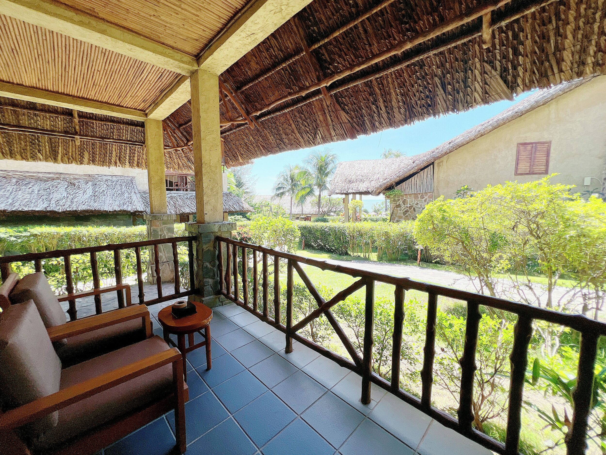 A covered outdoor area with a wooden bench and a small table, surrounded by a stone wall and a metal railing.