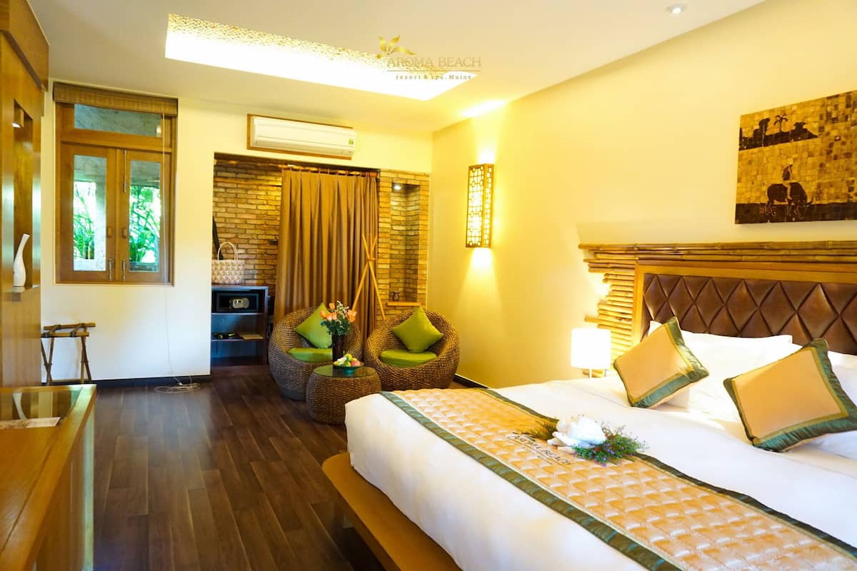 A hotel room with a bed, a seating area with chairs, a wooden desk, and a window with curtains.