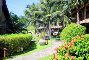 A tropical garden pathway leading to a building with thatched-roof structures.