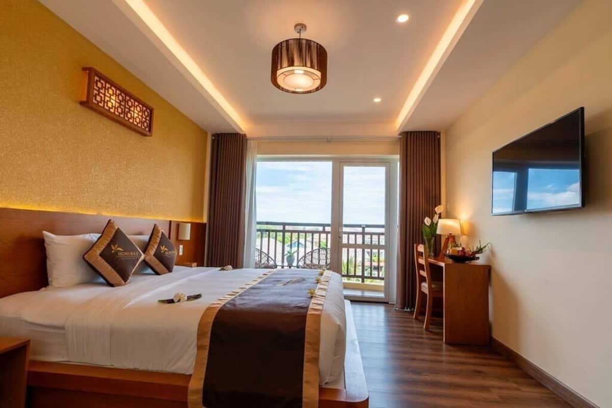 A hotel room with a large bed, a TV, a balcony with a view, and a ceiling light fixture.