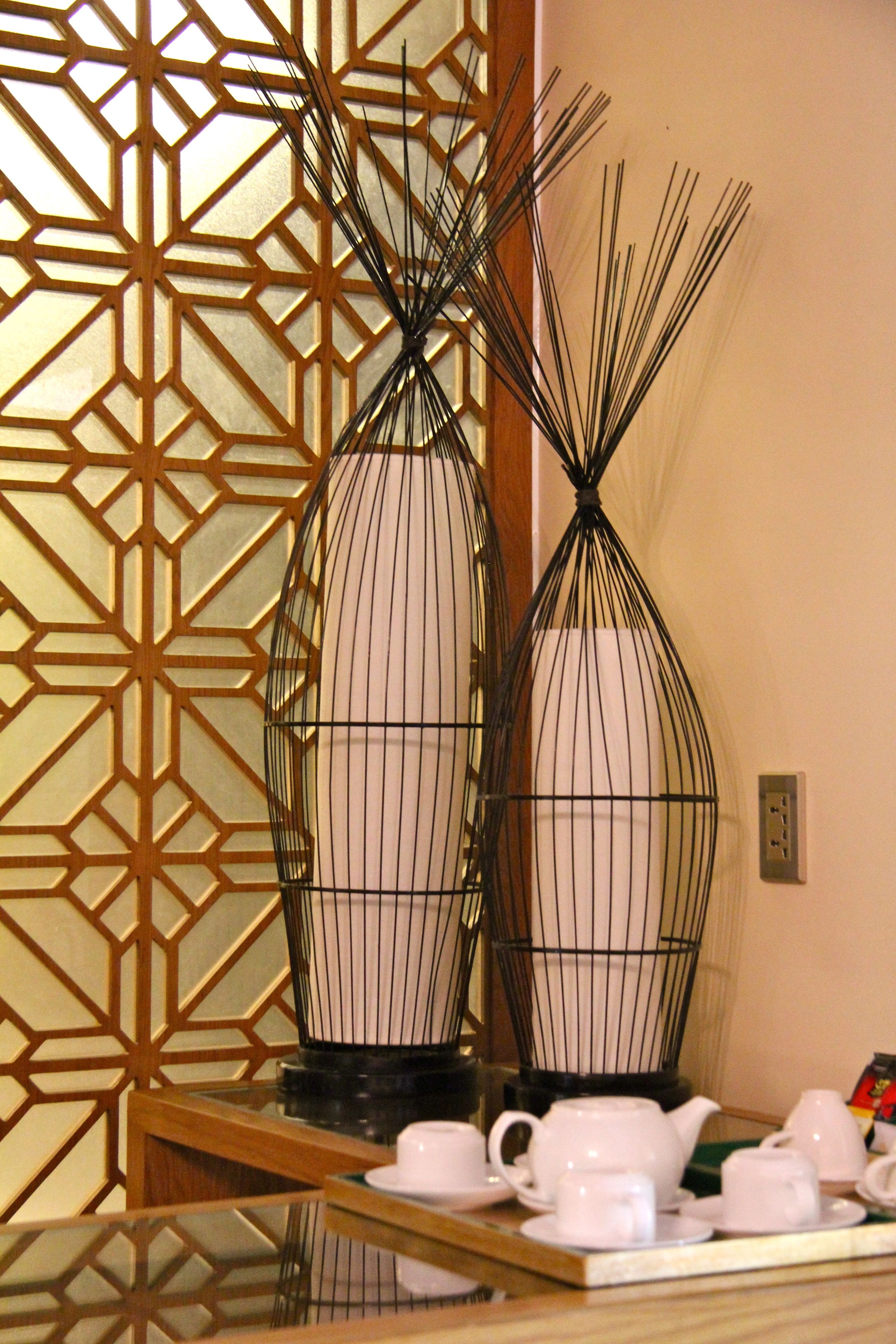 A room with a traditional Japanese-style partition with geometric patterns, a wooden table with white teacups and a teapot, and a decorative metal vase.