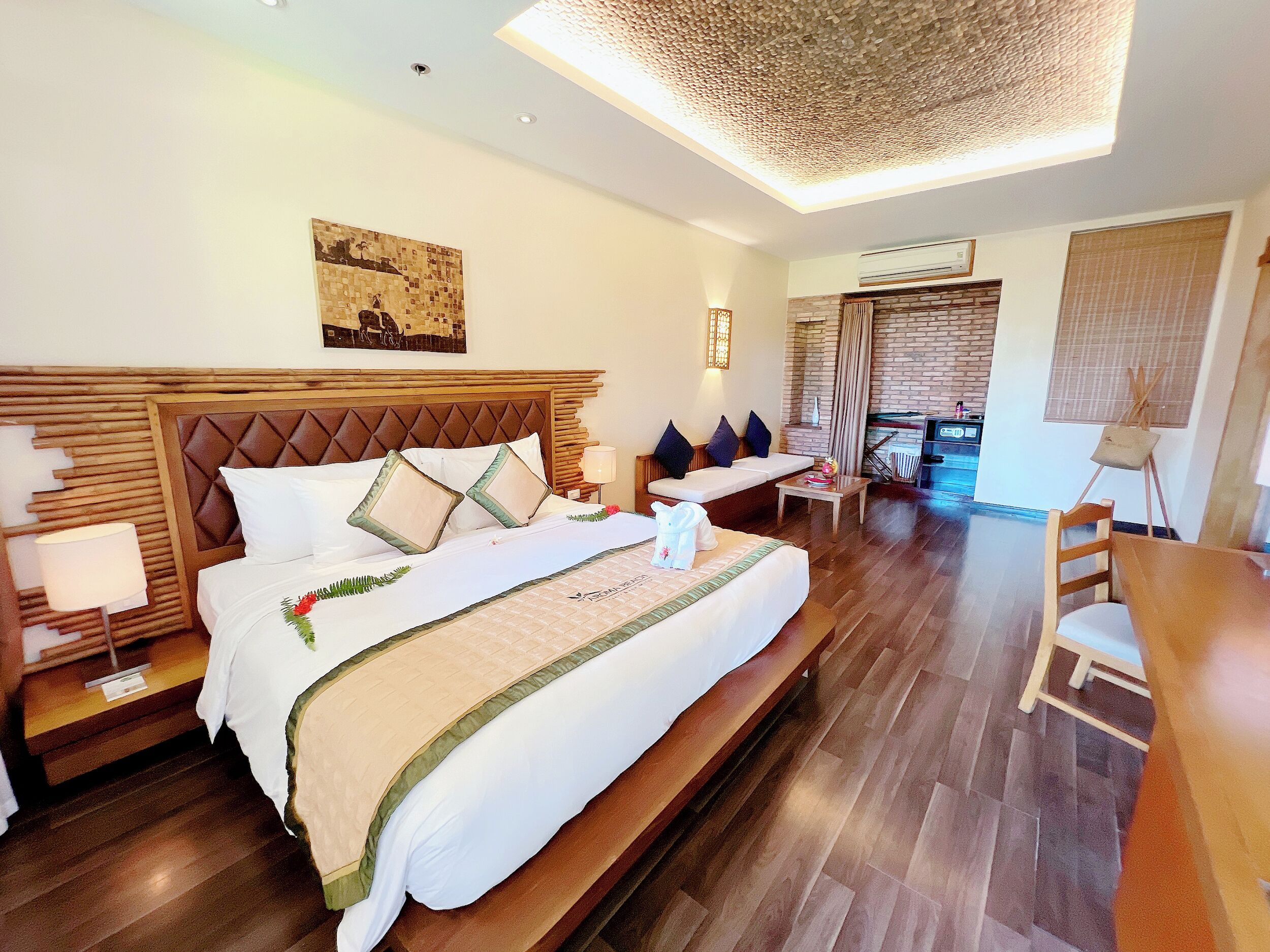 Amplia habitación de hotel con una cama grande, cabecera de madera, zona de comedor y vistas al exterior.