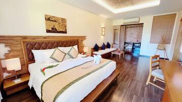 Amplia habitación de hotel con una cama grande, cabecera de madera, zona de comedor y vistas al exterior.