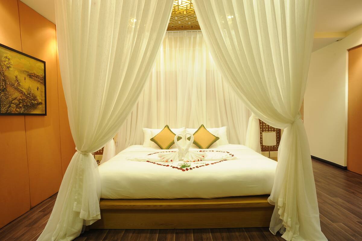 A bed with white bedding, two pillows, and a heart-shaped decoration made of flowers.