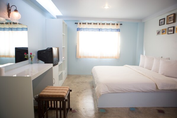 Un dormitorio con cama, escritorio y silla, televisor y ventana con cortinas.