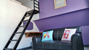 A room with a black leather sofa, two floral pillows, a framed picture on the wall, and a black metal ladder against a white and purple wall. - Dozy Lamoon House (Chiang Mai)