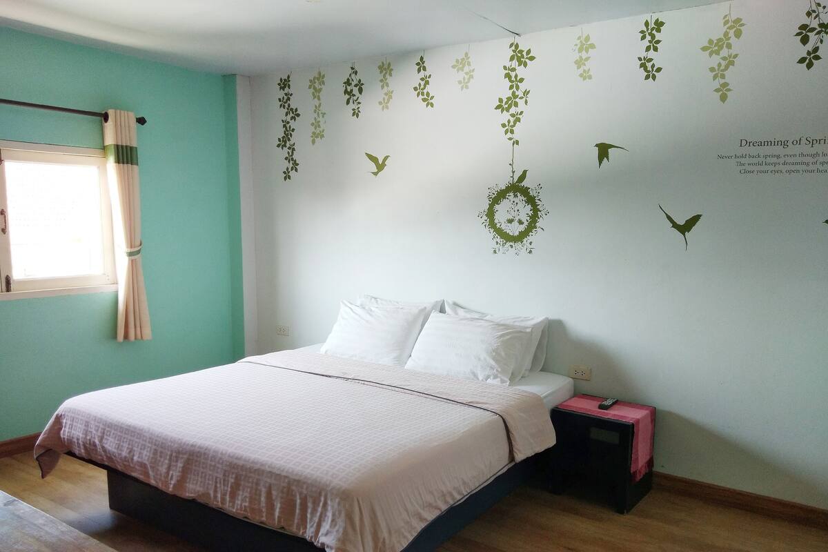 A bedroom with a bed, a nightstand, and a wall with decorative leaf and bird decals.