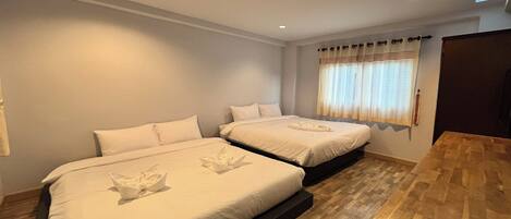 A hotel room with two beds, a wooden floor, a small table, and a window with curtains.