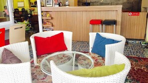 A reception area with a wooden counter, two red and black stools, and white wicker chairs with colorful cushions. - Dozy Lamoon House (Chiang Mai)