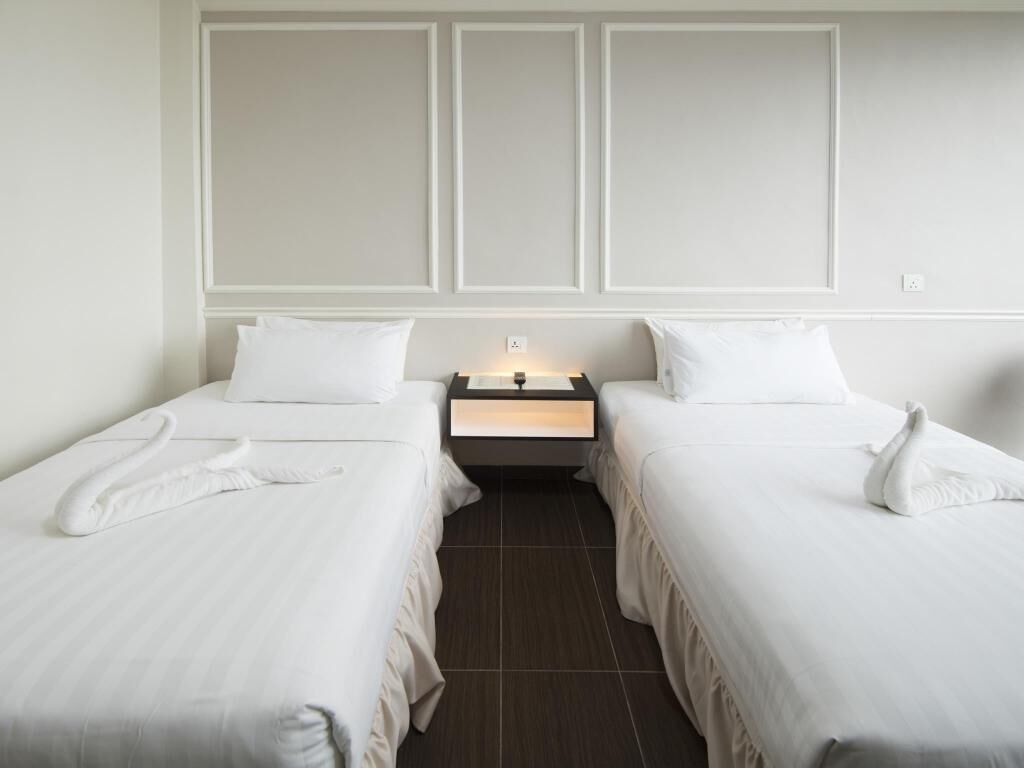 Habitación de hotel con dos camas individuales, una mesita de noche con lámpara y un diseño de panel en la pared.