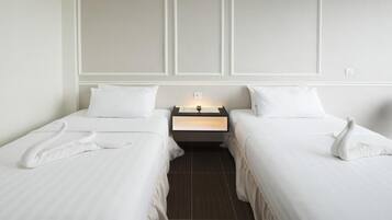 Habitación de hotel con dos camas individuales, una mesita de noche con lámpara y un diseño de panel en la pared.