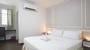 Habitación de hotel con cama, mesitas de noche, unidad de aire acondicionado, ventana con cortinas y un pequeño escritorio con silla.