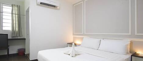 Habitación de hotel con cama, mesitas de noche, unidad de aire acondicionado, ventana con cortinas y un pequeño escritorio con silla.