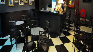 Un restaurante con suelo a cuadros blanco y negro, sillas negras y una barra con lámpara y fotografías enmarcadas.